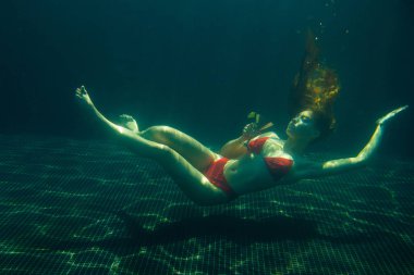 Güzel kızıl saçlı bir kadın suyun altında bir kokteyl ile poz veriyor..