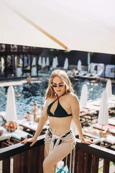 一位戴太阳镜 身穿泳衣的漂亮金发女子站在游泳池的后面 — 图库照片