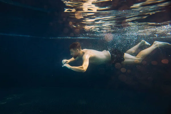 A young man swims underwater in a pool. Summer vacation concept.