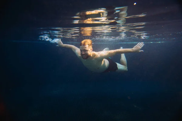 A young man swims underwater in a pool. Summer vacation concept.