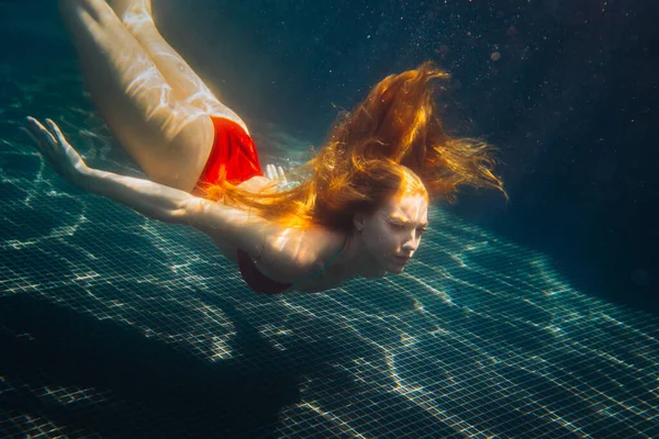 Genç kızıl saçlı kadın kaka içinde suyun altında yüzüyor.