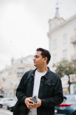 Genç Hintli bir adam sırt çantasıyla şehir caddesinde duruyor, cep telefonu kullanıyor, okuyor ve mesaj yazıyor, bir telefon görüşmesi yapıyor..