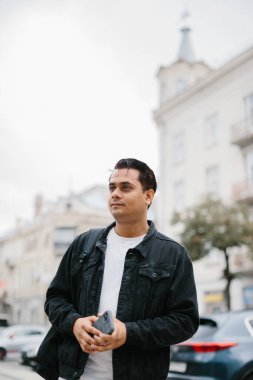 Genç Hintli bir adam sırt çantasıyla şehir caddesinde duruyor, cep telefonu kullanıyor, okuyor ve mesaj yazıyor, bir telefon görüşmesi yapıyor..