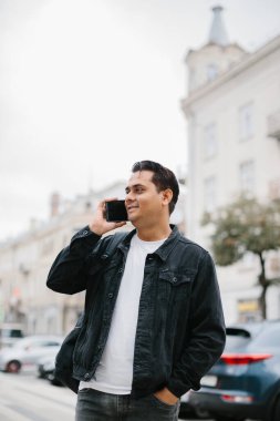 Genç Hintli bir adam sırt çantasıyla şehir caddesinde duruyor, cep telefonu kullanıyor, okuyor ve mesaj yazıyor, bir telefon görüşmesi yapıyor..