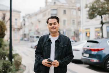 Elinde telefon olan mutlu bir Hintli turist şehrin sokaklarında yürüyor..