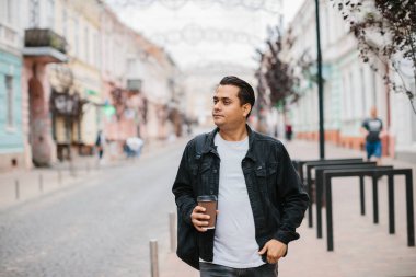 Elinde kahve ve sırt çantası olan mutlu bir Hintli turist şehir caddesinde yürüyor..