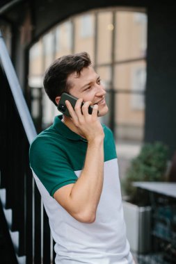 Neşeli genç adam sokakta telefonla konuşuyor..