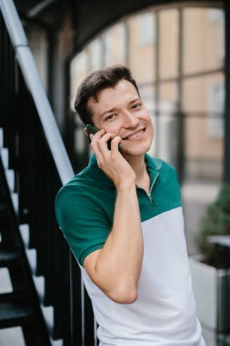 Neşeli genç adam sokakta telefonla konuşuyor..