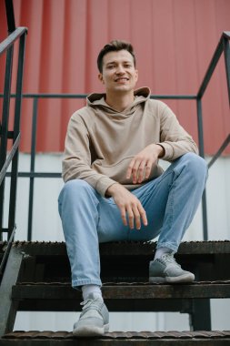 Caddedeki merdivenlerde oturan neşeli genç adam kameraya bakıyor..