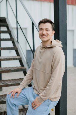 Caddedeki merdivenlerde oturan neşeli genç adam kameraya bakıyor..