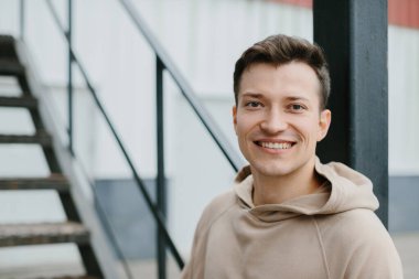 Caddedeki merdivenlerde oturan neşeli genç adam kameraya bakıyor..