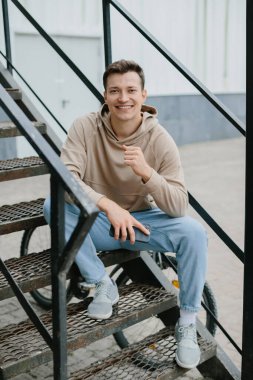 Caddedeki merdivenlerde oturan neşeli genç adam kameraya bakıyor..