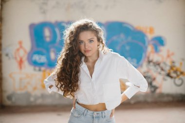 Grafiti duvarının arkasında poz veren kıvırcık saçlı şık bir genç kadın..