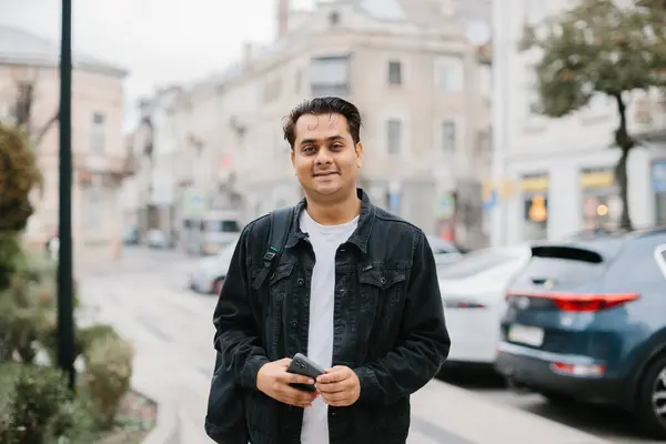 Elinde telefon olan mutlu bir Hintli turist şehrin sokaklarında yürüyor..