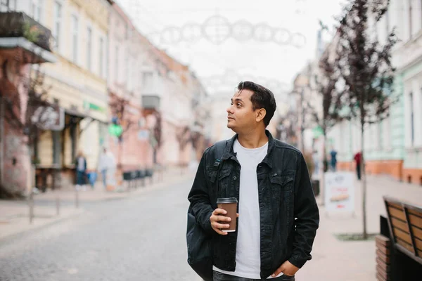 Elinde kahve ve sırt çantası olan mutlu bir Hintli turist şehir caddesinde yürüyor..