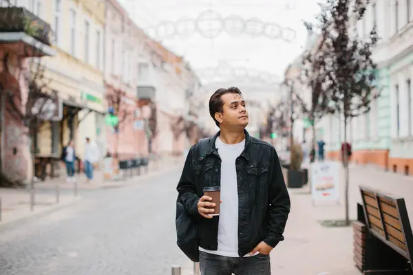 Elinde kahve ve sırt çantası olan mutlu bir Hintli turist şehir caddesinde yürüyor..