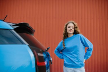 Şık bir genç kadın elektrikli arabasının yanında poz veriyor..