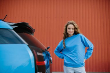 Şık bir genç kadın elektrikli arabasının yanında poz veriyor..