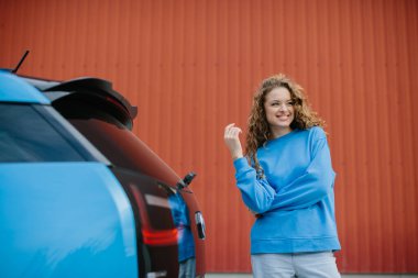 Şık bir genç kadın elektrikli arabasının yanında poz veriyor..