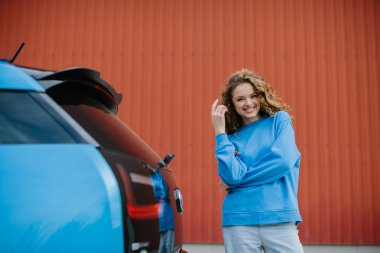 Şık bir genç kadın elektrikli arabasının yanında poz veriyor..