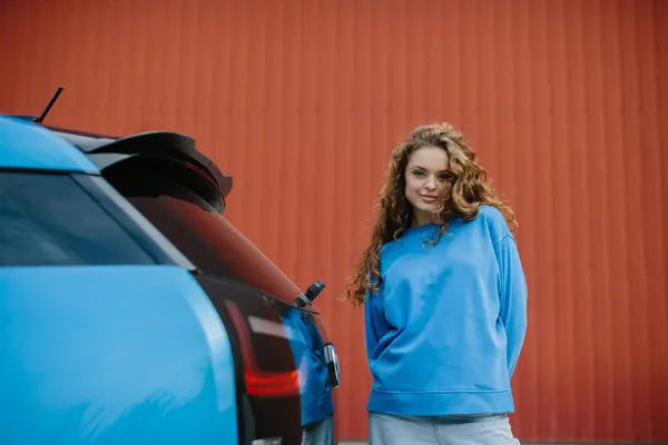 Stylowa Młoda Kobieta Stoi Obok Swojego Elektrycznego Samochodu Parkingu — Zdjęcie stockowe