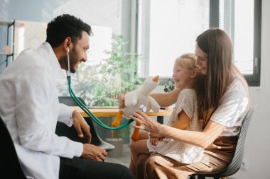 Çocuk doktoru çocukla iletişim, güven ve iyi bir ilişki kurar. Mutlu küçük kız, anne ve aile doktoru oyuncaklar ve steteskopla oyun oynuyorlar.