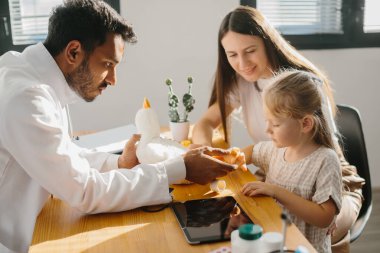 Bir çocuk doktoru bir çocuk hastayla temas kurar. Anaokulu kızı, doktor randevusunda pelüş bir oyuncak ve yara bandıyla oynar..