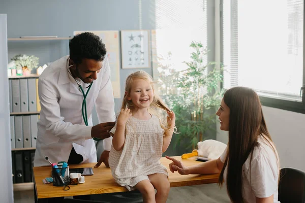 母親と子供は家族の実践者を見ています 小さな女の子の肺をチェックするステスコープを持つ小児科医の笑顔 — ストック写真