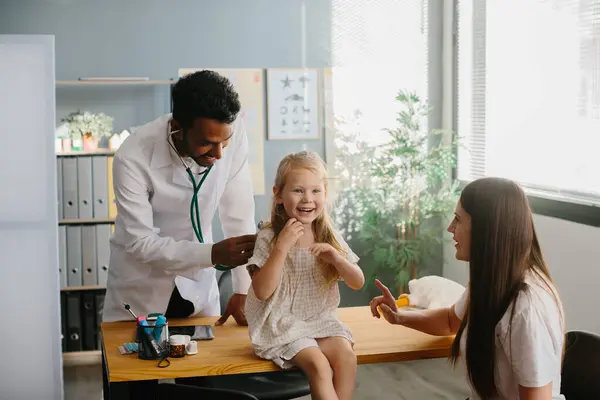 母親と子供は家族の実践者を見ています 小さな女の子の肺をチェックするステスコープを持つ小児科医の笑顔 — ストック写真