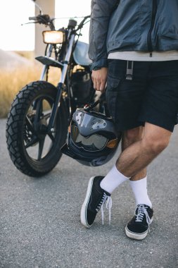 Bir motorcu gün batımında arka planda bir kaskı elinde tutar..