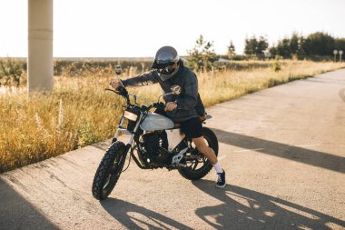 Motosikletli adam şehir dışında yolda, gün batımında..