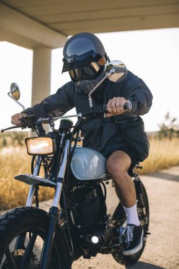 Günbatımında otoyolda klasik motosikletli bir adam. Bir adam kafe yarışçısı sürüyor. Bisikletçi yaşam tarzı konsepti