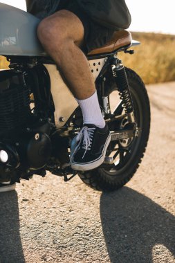 Günbatımında otoyolda klasik motosikletli bir adam. Bir adam kafe yarışçısı sürüyor. Bisikletçi yaşam tarzı konsepti