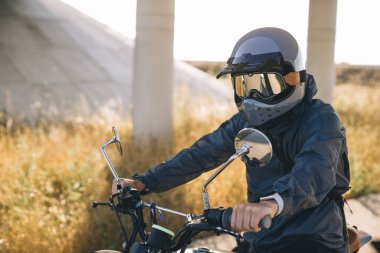 Günbatımında otoyolda klasik motosikletli bir adam. Bir adam kafe yarışçısı sürüyor. Bisikletçi yaşam tarzı konsepti