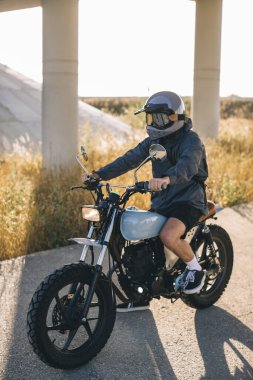 Günbatımında otoyolda klasik motosikletli bir adam. Bir adam kafe yarışçısı sürüyor. Bisikletçi yaşam tarzı konsepti