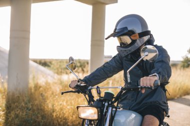 Günbatımında otoyolda klasik motosikletli bir adam. Bir adam kafe yarışçısı sürüyor. Bisikletçi yaşam tarzı konsepti