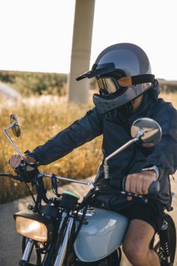 Günbatımında otoyolda klasik motosikletli bir adam. Bir adam kafe yarışçısı sürüyor. Bisikletçi yaşam tarzı konsepti