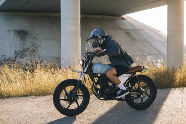 Günbatımında otoyolda klasik motosikletli bir adam. Bir adam kafe yarışçısı sürüyor. Bisikletçi yaşam tarzı konsepti