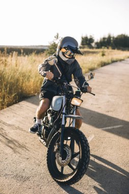 Günbatımında otoyolda klasik motosikletli bir adam. Bir adam kafe yarışçısı sürüyor. Bisikletçi yaşam tarzı konsepti