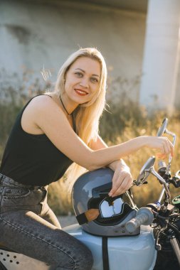 Motosikletli kız motosiklete biner. Gün batımında otobanda motosiklette oturan güzel sarışın kadın..
