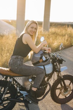 Motosikletli kız motosiklete biner. Gün batımında otobanda motosiklette oturan güzel sarışın kadın..