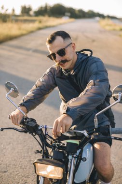 Motosikletli adam kontak anahtarını çevirerek motorunu çalıştırıyor. Gün batımında motosiklet sürme kavramı.