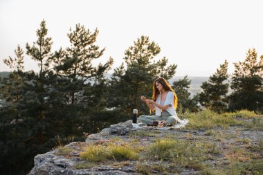 Genç bir kadın elinde tütsü sopasıyla meditasyon yaparken gün batımında bir kayanın üzerinde oturuyor..