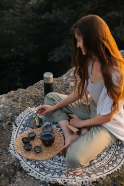 Genç bir kadın elinde tütsü sopasıyla meditasyon yaparken gün batımında bir kayanın üzerinde oturuyor..
