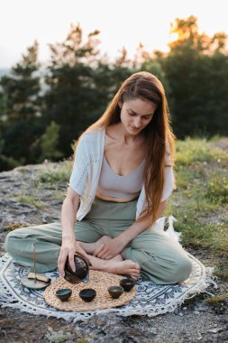 Genç ve güzel bir kadın gün batımında dağlarda Çin çay seremonisi yapar..