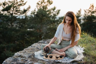 Genç ve güzel bir kadın gün batımında dağlarda Çin çay seremonisi yapar..