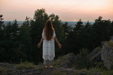 Eğlence ve doğa ile birlik kavramı. Genç bir kadın, batan güneşin arka planında meditasyon yapıyor..