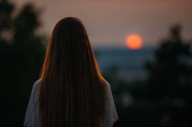 Eğlence ve doğa ile birlik kavramı. Genç bir kadın, batan güneşin arka planında meditasyon yapıyor..