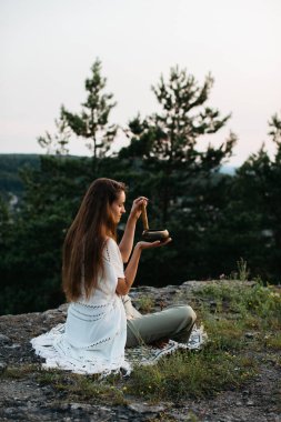 Genç ve güzel bir esmer kadın, batan güneşin ışınlarında, bir çam ormanının arka planında meditasyon yapıyor..