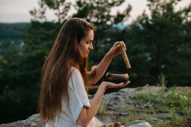 Genç ve güzel bir esmer kadın, batan güneşin ışınlarında, bir çam ormanının arka planında meditasyon yapıyor..